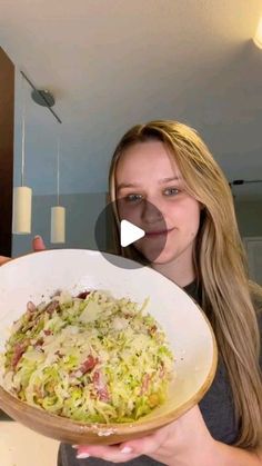 a woman holding up a bowl filled with coleslaw in her hand and pointing to the camera