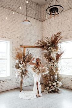 a woman in a white dress standing next to an arch with flowers and greenery