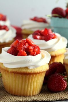 several cupcakes with white frosting and strawberries on the top are sitting on a table