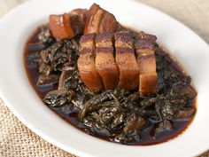 a white plate topped with meat and greens covered in gravy on top of a table