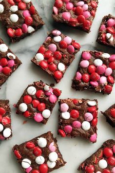 chocolate brownies with red, white and pink candies on top are arranged on a marble surface