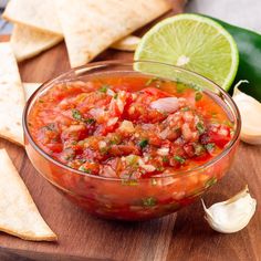 a glass bowl filled with salsa and tortilla chips on top of a wooden cutting board