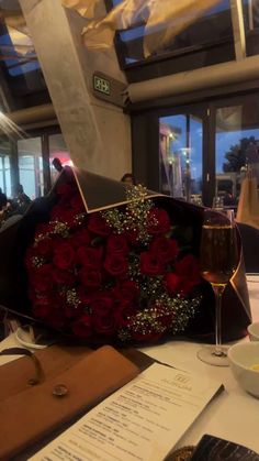 a bouquet of red roses sitting on top of a table next to a glass of wine