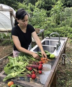 a woman is cutting vegetables on a table in the garden with a sink behind her