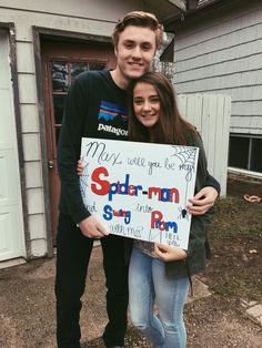 a man and woman holding up a sign in front of a house that says spider - man