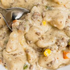 a white bowl filled with meat and veggies covered in gravy next to a spoon