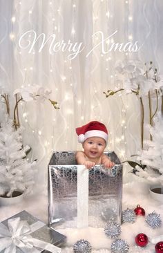 a baby wearing a santa hat sitting in a box surrounded by christmas decorations and presents