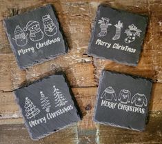 four slate coasters with christmas designs on them sitting on top of a wooden table