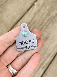 a hand holding a small metal tag with the word moose on it's side