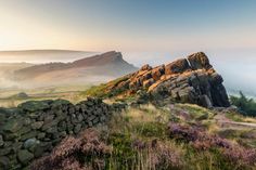 a rocky hill with grass and rocks in the foreground on a foggy day