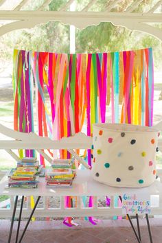 a white table topped with lots of books under a colorful streamer curtain covered in confetti