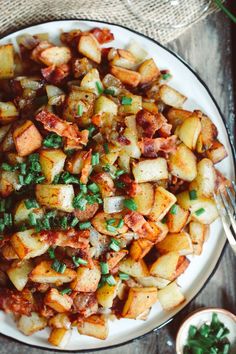 a white plate topped with potatoes covered in seasoning next to a bowl of greens