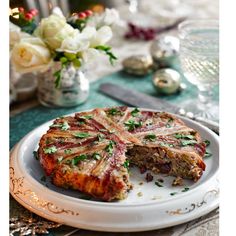 a white plate topped with meat and veggies next to a vase filled with flowers