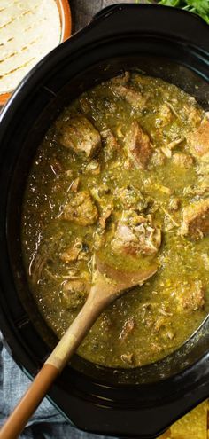 a black crock pot filled with chicken and green sauce next to tortilla chips