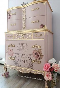 a pink dresser sitting on top of a hard wood floor next to a vase with flowers