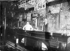 two men are standing at the bar in an old time pub, one man is behind the counter