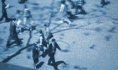 people are walking on the sidewalk in front of a building with blue tinted glass covering it