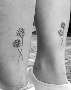 black and white photo of two flower tattoos on the legs, both with one single daisy