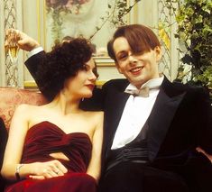 a man in a tuxedo sitting next to a woman wearing a red dress