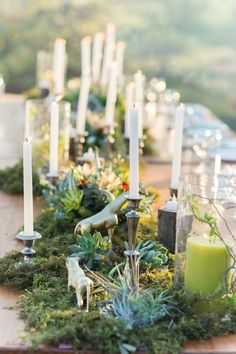 a long table with candles and succulents on it, surrounded by greenery