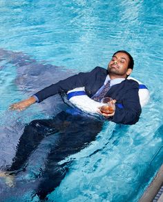 a man in a suit and tie is floating on an inner tube while holding a drink