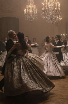 two people in formal dress dancing on the dance floor with chandeliers hanging from the ceiling