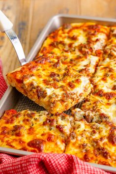 a pan filled with pizza sitting on top of a wooden table next to a red and white checkered cloth