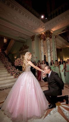 a man kneeling down next to a woman in a pink dress