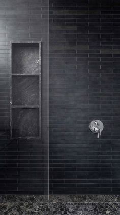 a black and white photo of a shower in a bathroom with dark tiles on the walls