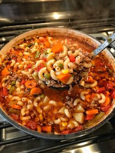 a pot filled with pasta and vegetables on top of an oven burner next to a stove