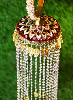 Traditional Indian bridal jewelry does not just carry stories of cultural value. But, also adds a touch of elegance to the bride's outfit. Gold-plated Kalira bangle jewelry comes with cluster pearl bands. Red Meenakari work accents this Kaleereh adding color to this bride's jewelry. Multiple leaf-like metal carvings adorn this Kaleera, making it the perfect piece for your Indian Kalire ceremony. Strands of mini-pearl hangings further elaborated with Butta jewelry at the bottom make it one of a k Festive Bridal Sets With Latkans For Diwali, Pearl Bridal Earrings With Meenakari For Celebration, White Meenakari Bridal Earrings, Latkan Round Bead Earrings For Weddings, White Meenakari Bridal Earrings For Wedding, Bridal Earrings With Latkans For Navratri Wedding, Festive Bridal Pearl Earrings With Meenakari, Traditional White Bridal Sets For Ceremonial Occasions, Festive Pearl Bridal Earrings With Stone Work