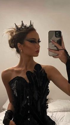 a woman taking a selfie with her cell phone wearing a black dress and tiara