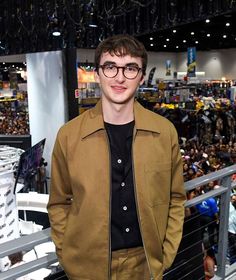 a young man wearing glasses standing in front of a crowd