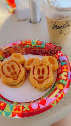 two mickey mouse waffles on a colorful plate next to a cup of coffee