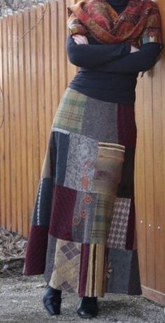 a woman leaning against a wooden fence wearing a long skirt with patchwork on it