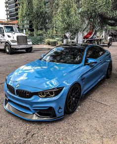 a blue bmw is parked in front of a tree and some other vehicles on the street