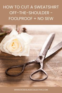 a pair of scissors sitting on top of a wooden table next to a white rose