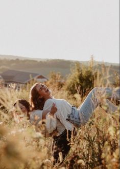 two women are laying in tall grass and one is holding the other woman's back