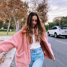 a woman walking down the street wearing jeans and a pink cardigan jacket with her arms outstretched