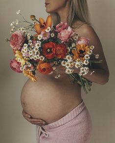 a pregnant woman with flowers on her belly holding a bouquet of flowers in front of her stomach