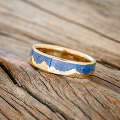 a gold ring with blue opal inlays sitting on top of a wooden surface