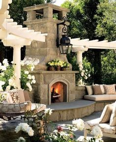 an outdoor fireplace with lots of seating around it and flowers on the table next to it