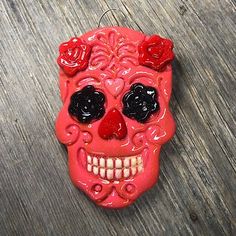 a red sugar skull ornament with black eyes and roses on its head, sitting on a wooden surface