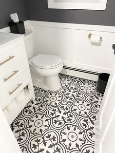 a white toilet sitting next to a sink in a bathroom under a window on top of a tiled floor