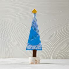 a small blue glass christmas tree on top of a wooden stand against a white wall