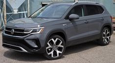 a grey volkswagen suv parked in front of a blue building with graffiti on the walls