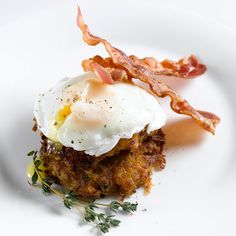 a white plate topped with an egg and bacon hashbrowns covered in sauce