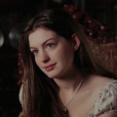 a woman with long hair sitting in a chair looking at the camera while wearing a necklace