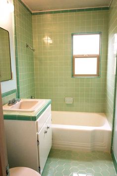 a bathroom with green tiles on the walls and white fixtures, including a tub, sink, and toilet