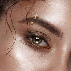 a close up shot of a woman's eye with gold jewelry on her forehead